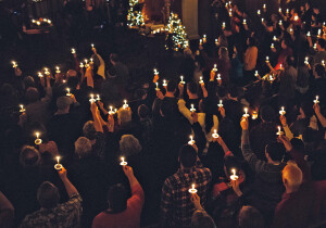 A large group of people in a church congregation hold lighted candles aloft during a time of celebration on the eve of Christmas day, the final day of advent.